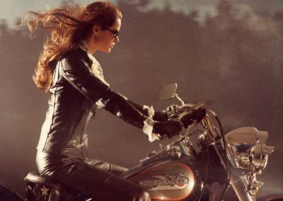 femme brune habillée en cuir noir, sur une moto, les cheveux au vent